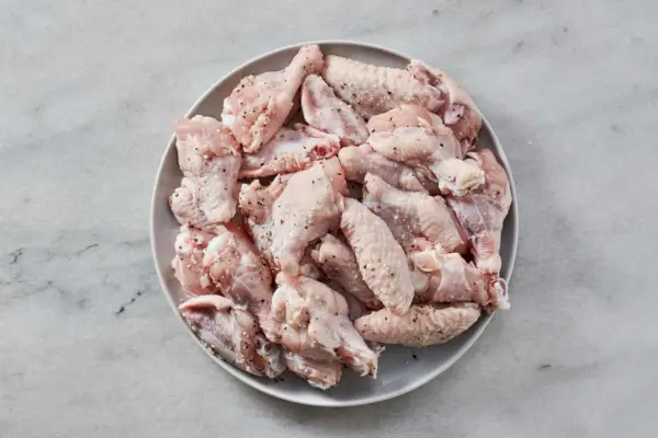 Un plato grande de alitas de pollo crudas cubiertas con sal y pimienta.