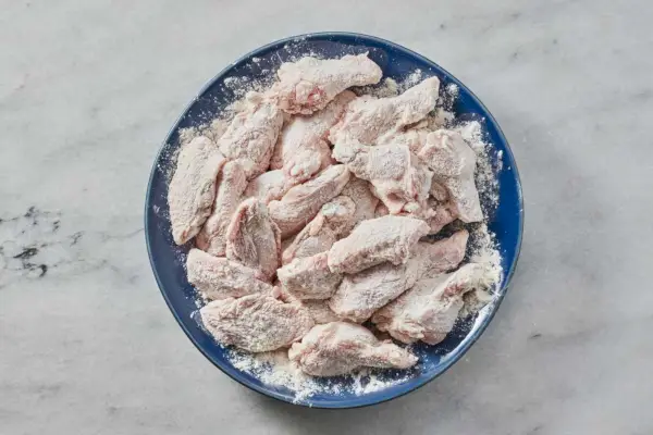 Un plato grande de alitas de pollo crudas bañadas en harina