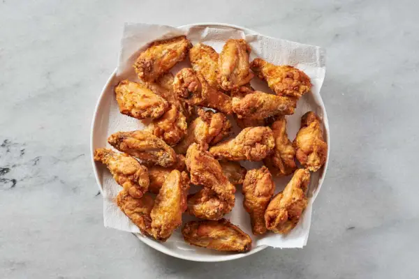 Un plato grande forrado con toallas de papel con alitas de pollo fritas crujientes