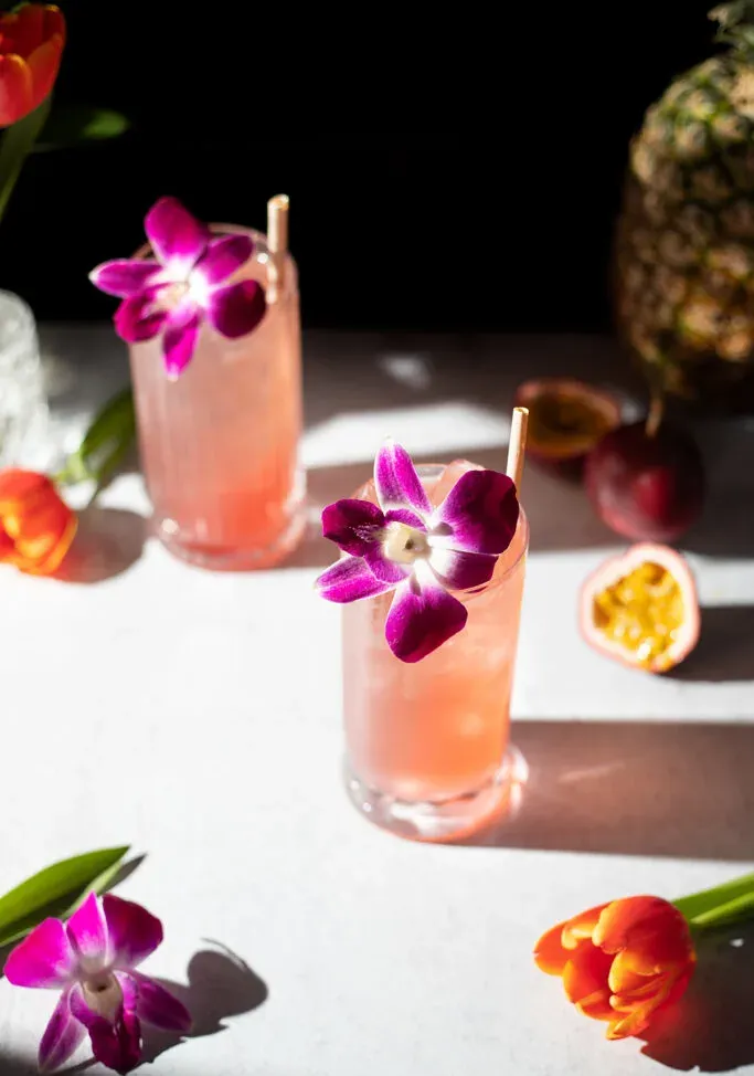 zwei große rosa Getränke neben Blumen und Passionsfrucht.' title=