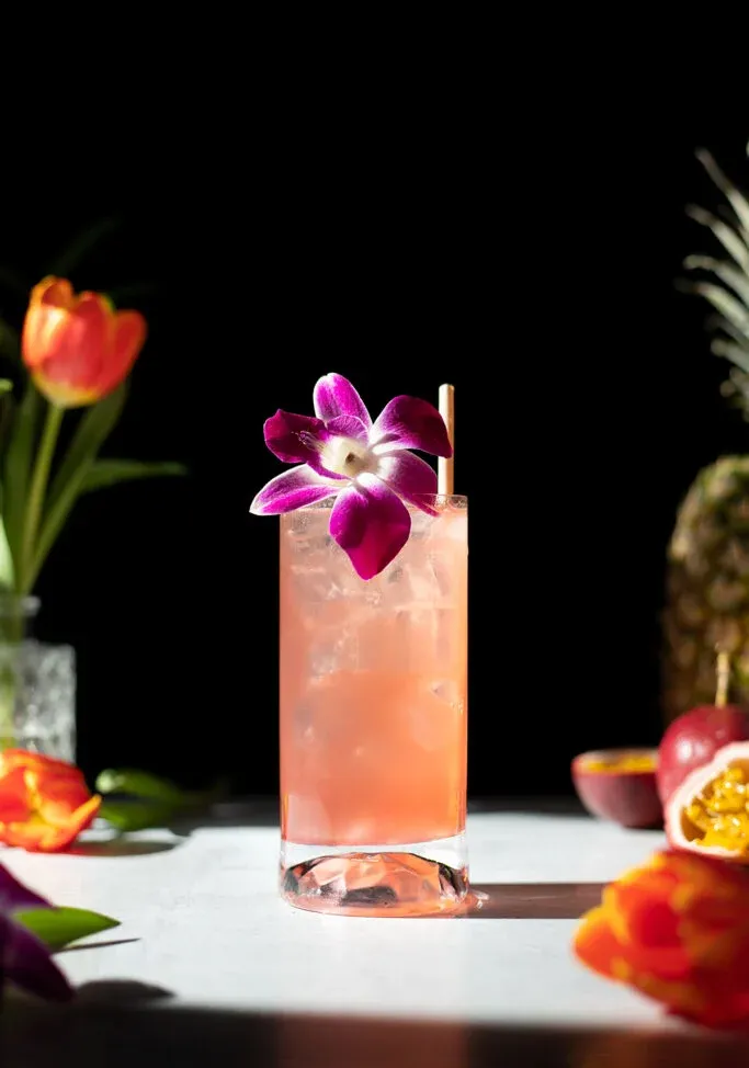 großes rosafarbenes Getränk neben roter Tulpe und Ananas.' title=