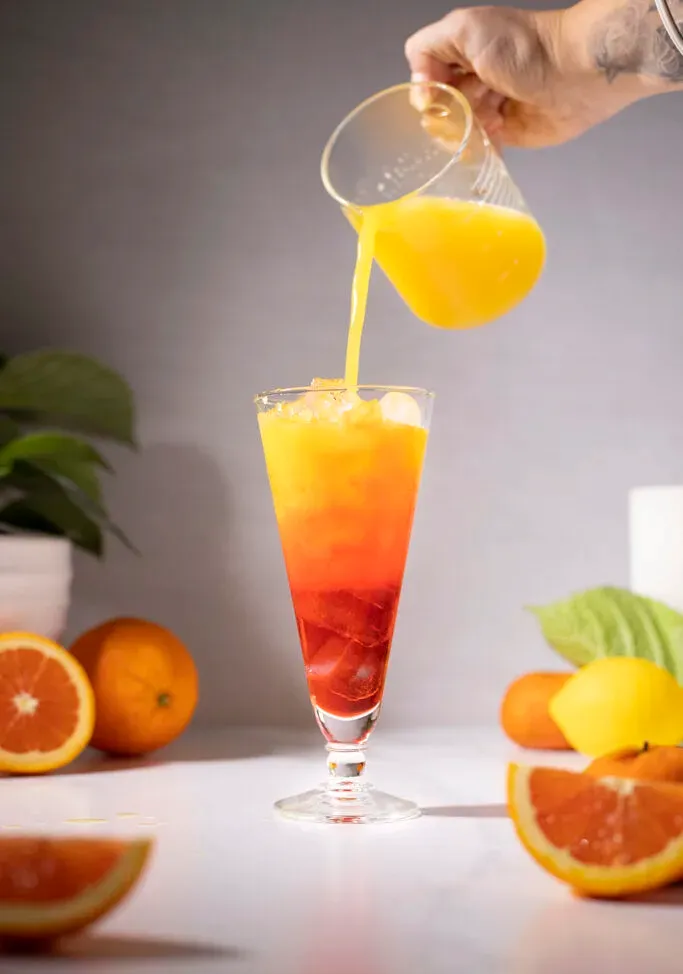 verser du jus d'orange d'un pichet dans une boisson rouge.' loading='lazy' title=