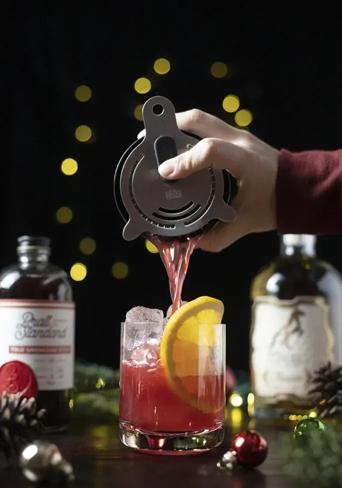 vertiendo una bebida roja de una coctelera en un vaso bajo lleno de hielo.' loading='lazy' title=