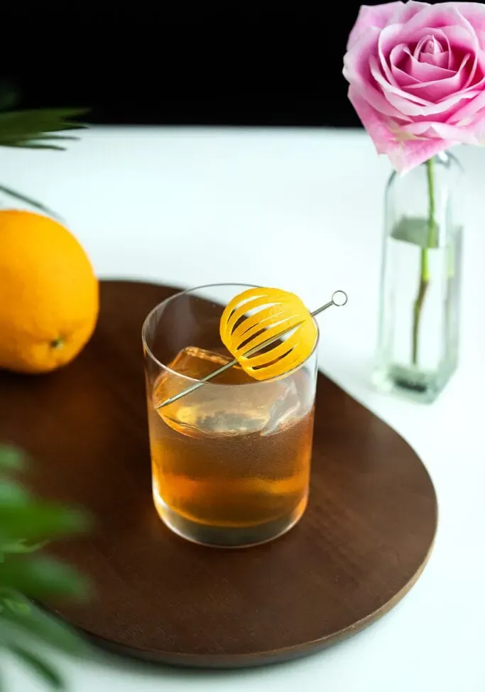 오렌지 껍질을 얹은 바위 잔에 위스키 칵테일을 곁들인 것.' title=