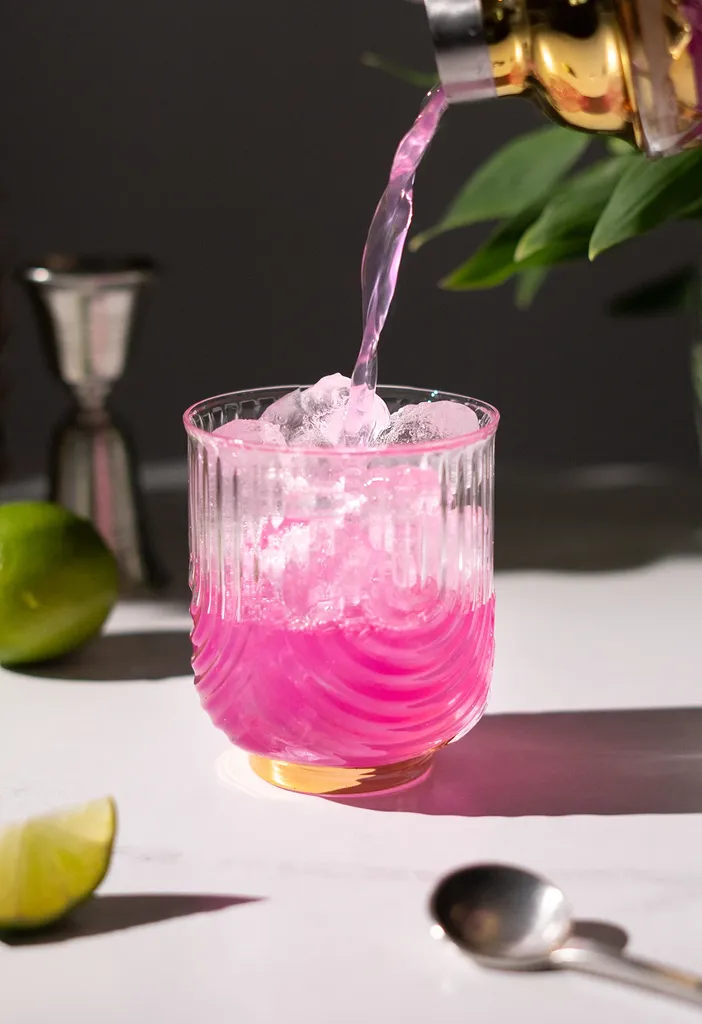カクテルシェーカーから氷を入れたロックグラスに明るいピンク色の液体を注ぎます。' loading='lazy' title=