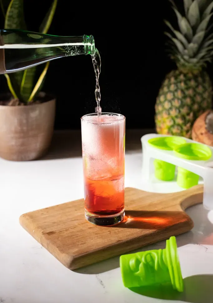 שפיכת מים מוגזים למשקה אדום גבוה.' loading='lazy' title=