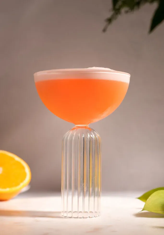 pomarančový koktail s bielou penou navrchu v pohári na kupé.' loading='lazy' title=