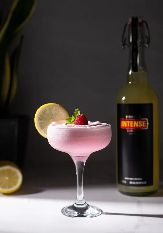 כוס מלאה במשקה ורוד מוקצף לצד בקבוק ליקר ג'ינג'ר אינטנסיבי של בארו.' loading='lazy' title=