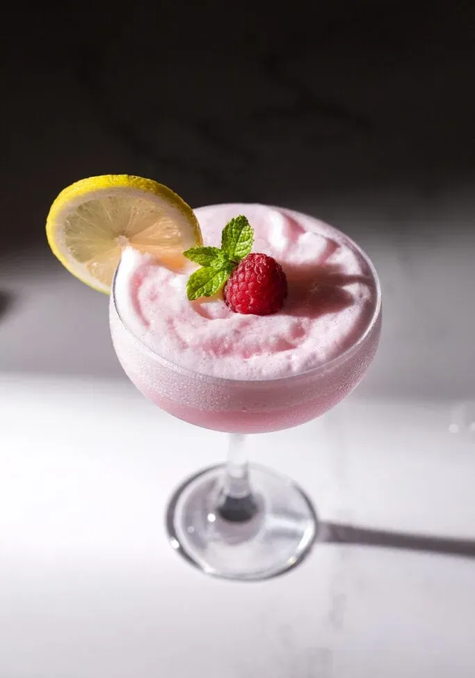 תקריב של כוס קופה מלאה בקוקטייל מוקצף ורוד.' title=