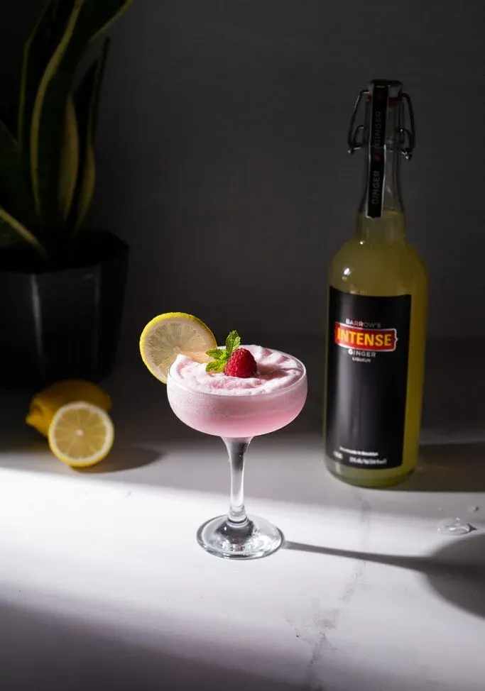 שולחן שיש עם קוקטייל ורוד בקבוק ליקרים לימונים וצמח.' title=