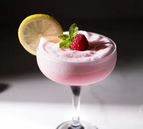 כוס קופה מלאה במשקה ורוד עם גלגל לימון.' title=