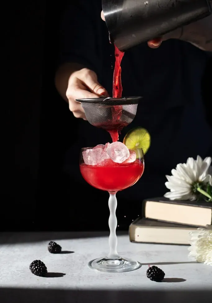 Einen leuchtend roten Cocktail in ein Stielglas abseihen' title=