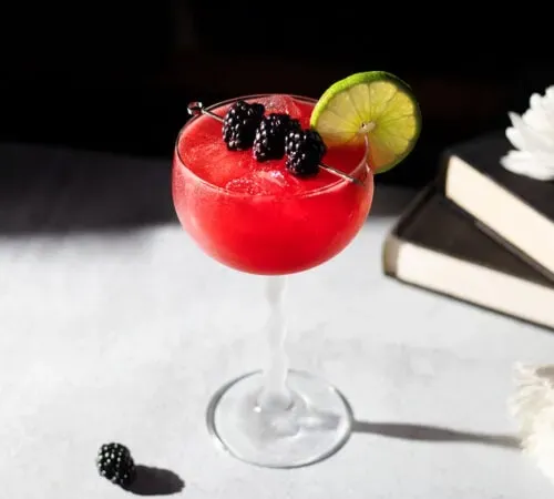ein leuchtend rotes Getränk in einem Stielglas, garniert mit Brombeeren' title=