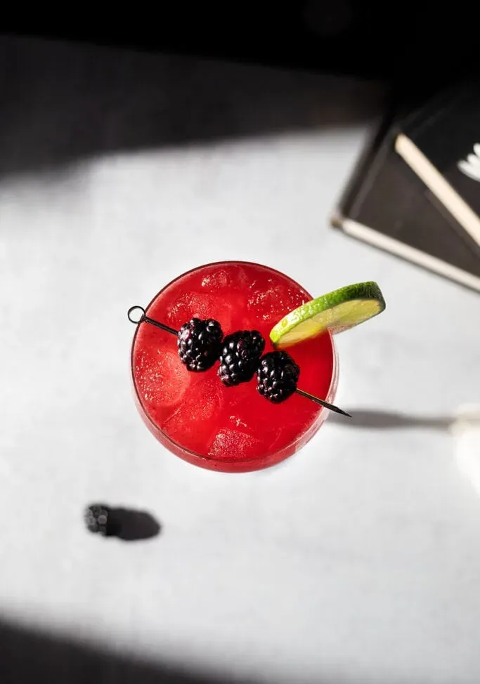 Blick von oben auf ein rotes Getränk, garniert mit frischen Brombeeren und Limette' title=