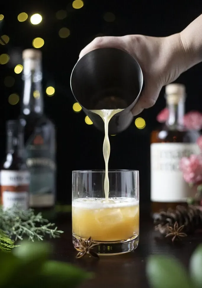 vertiendo una bebida de color amarillo pálido de una coctelera de metal en un vaso bajo.' loading='lazy' title=