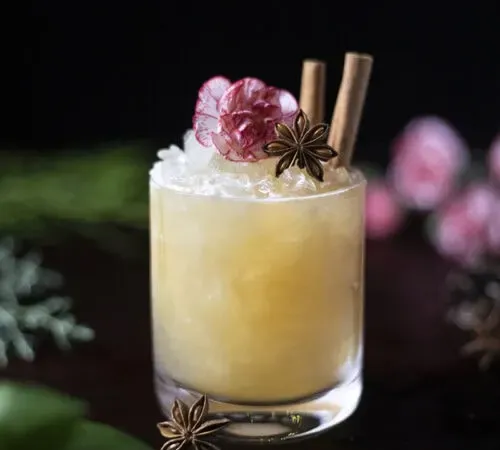 cóctel amarillo en un vaso bajo con hielo picado, anís estrellado y ramas de canela' title=