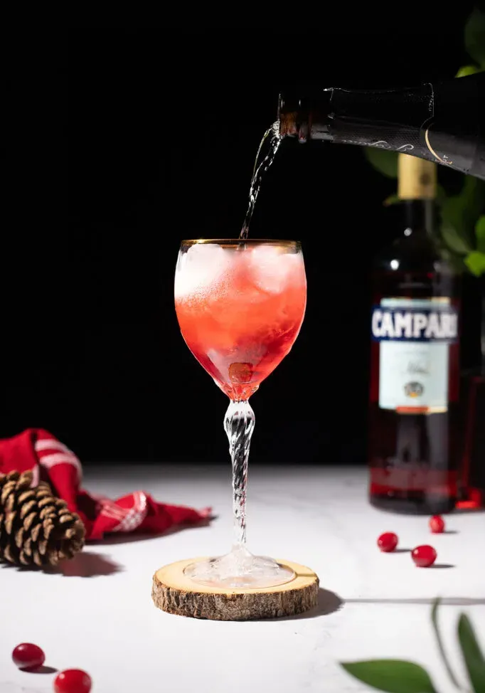 versare il prosecco in un bicchiere da vino colmo di liquido rosso e ghiaccio.' loading='lazy' title=