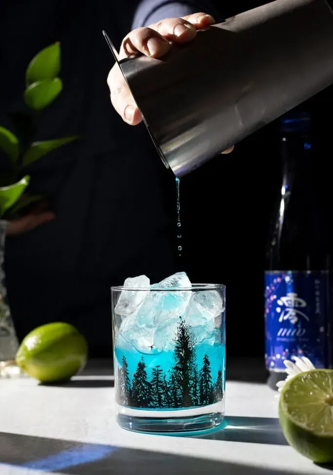 nalewając niebieski napój do szklanki wypełnionej lodem.' loading='lazy' title=