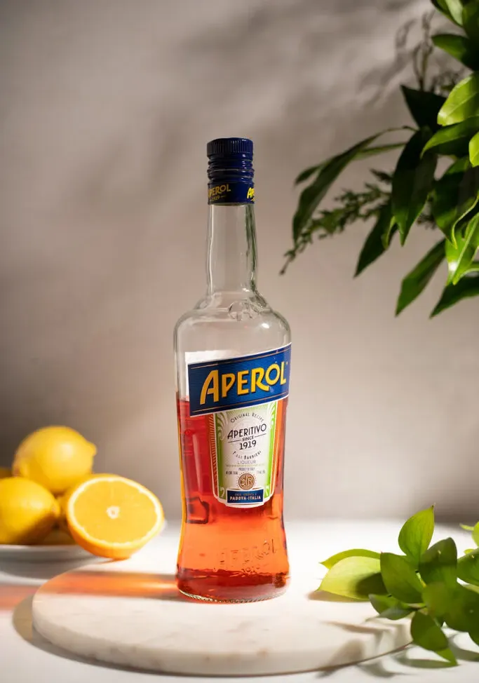 bottiglia di Aperol su un vassoio di marmo con foglie arancioni e verdi.' loading='lazy' title=