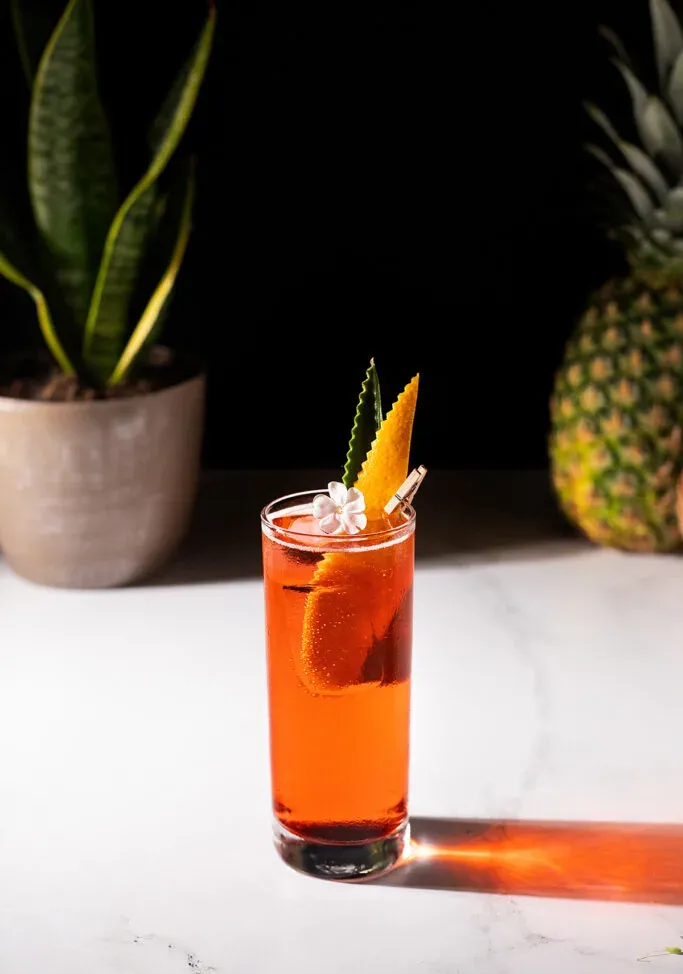 햇빛 아래 하얀 테이블 위에 놓인 키가 큰 빨간 음료.' title=