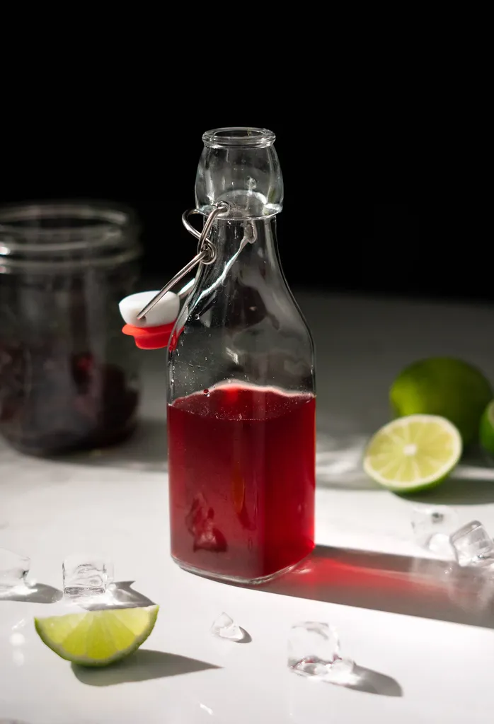 בקבוק זכוכית חצי מלא בנוזל אדום ליד טריז ליים.' loading='lazy' title=