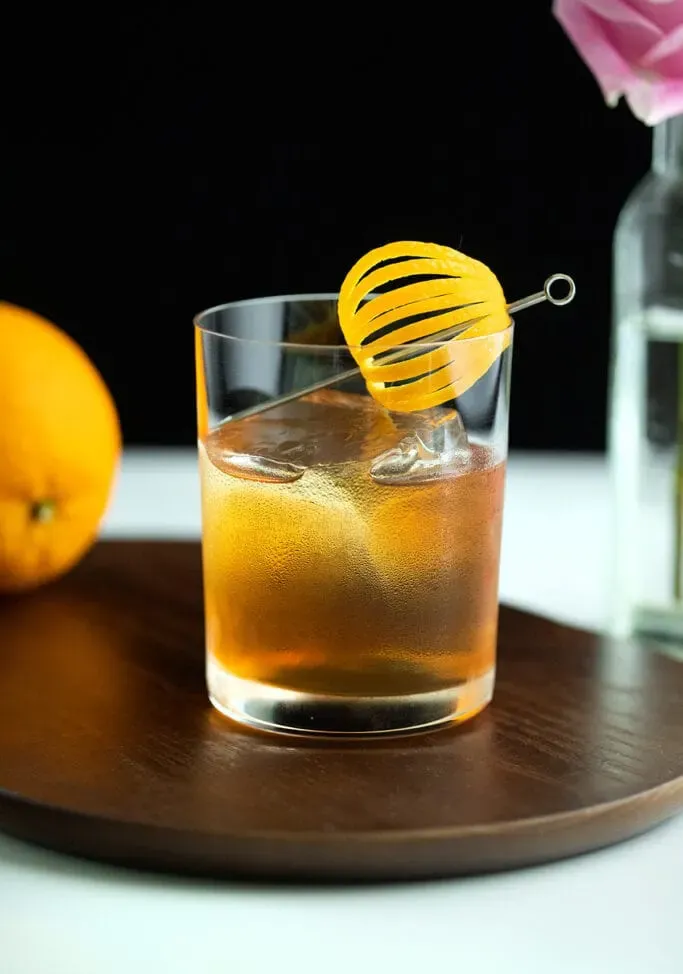 un cóctel de whisky en un vaso bajo con una elegante piel de naranja.' title=
