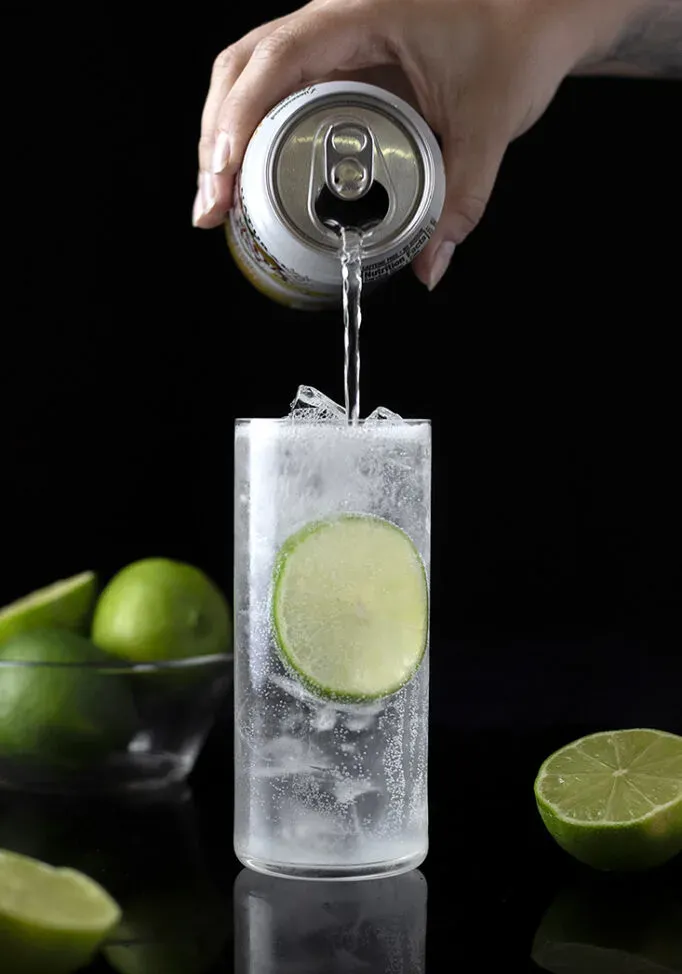 verter agua mineral en un vaso alto con ginebra y jugo de limón' loading='lazy' title=