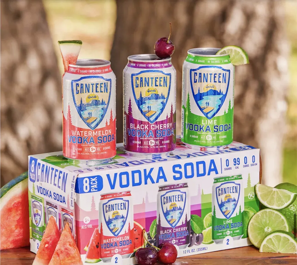 Cantina Vodka Soda caja de embalaje con tres latas encima rodeadas de fruta.' title=