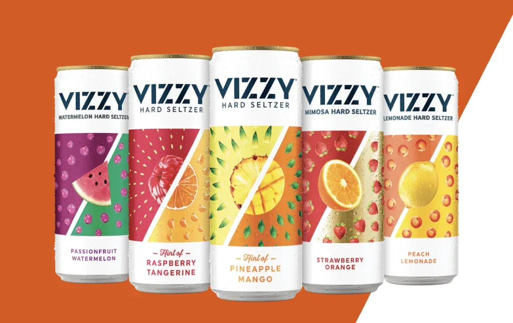 Cinco latas de agua mineral dura VIZZY sobre un fondo naranja y blanco.' title=