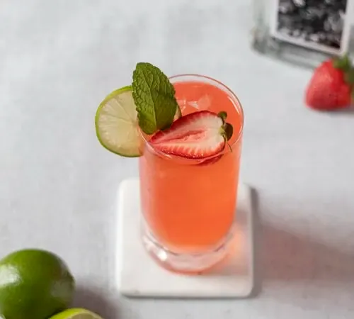 Vista de arriba hacia abajo de un cóctel de color naranja con fresas y lima' title=