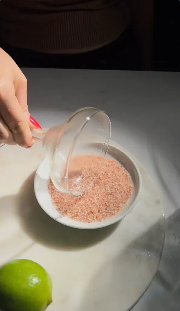 מחזיק את קצה כוס מרגריטה בצלחת רדודה של מלח ורוד.' loading='lazy' title=