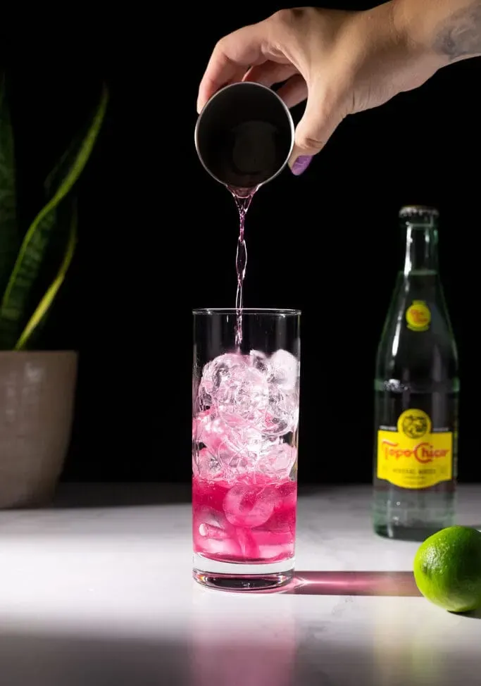 vertiendo tequila con infusión de arándanos en un vaso alto.' loading='lazy' title=