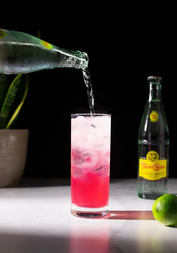 vertiendo agua mineral Topo Chico en un vaso alto.' title=