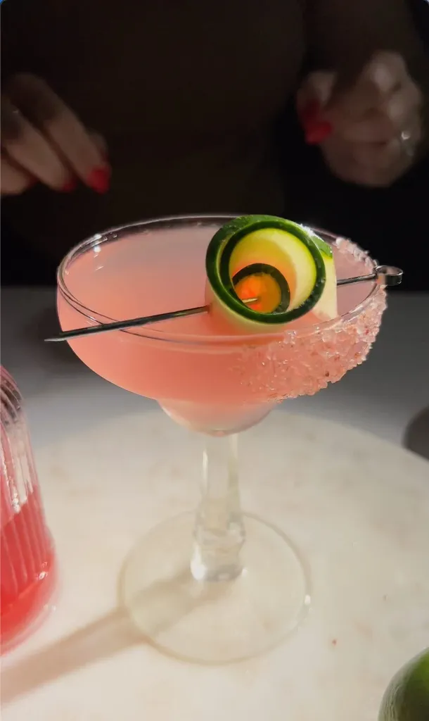 liquido rosa in un bicchiere da margarita guarnito con anguria arrotolata e infilzata su uno stecchino da cocktail.' title=