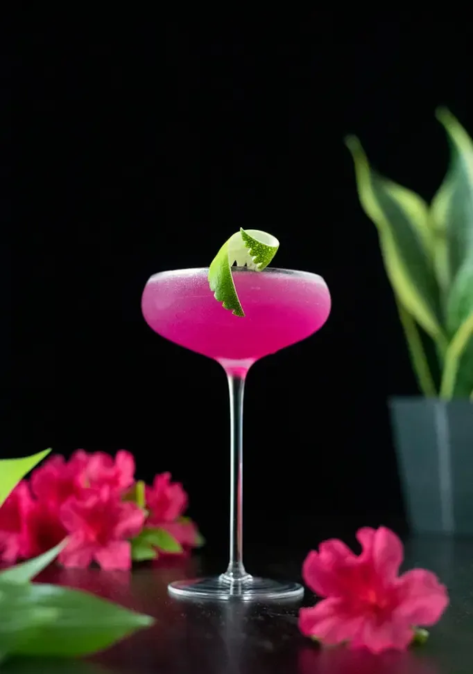 ライムのツイストを添えた背の高いクーペ グラスに入ったネオン ピンクのカクテル' title=