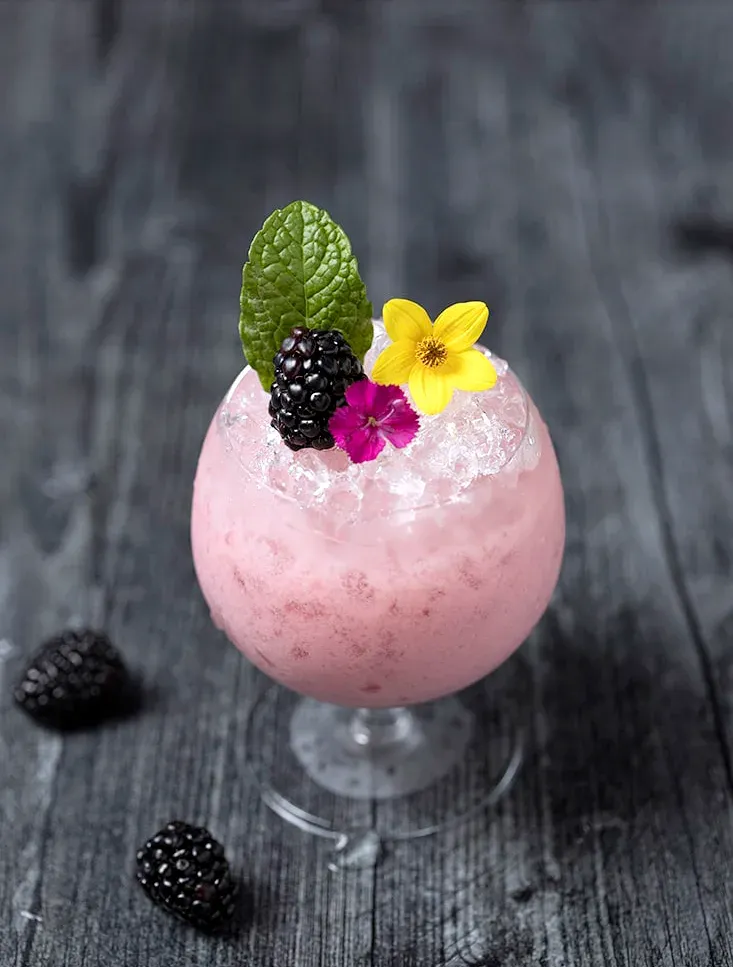 Nahaufnahme einer Getränkegarnitur mit essbaren Brombeerblüten und Minzblättern.' loading='lazy' title=
