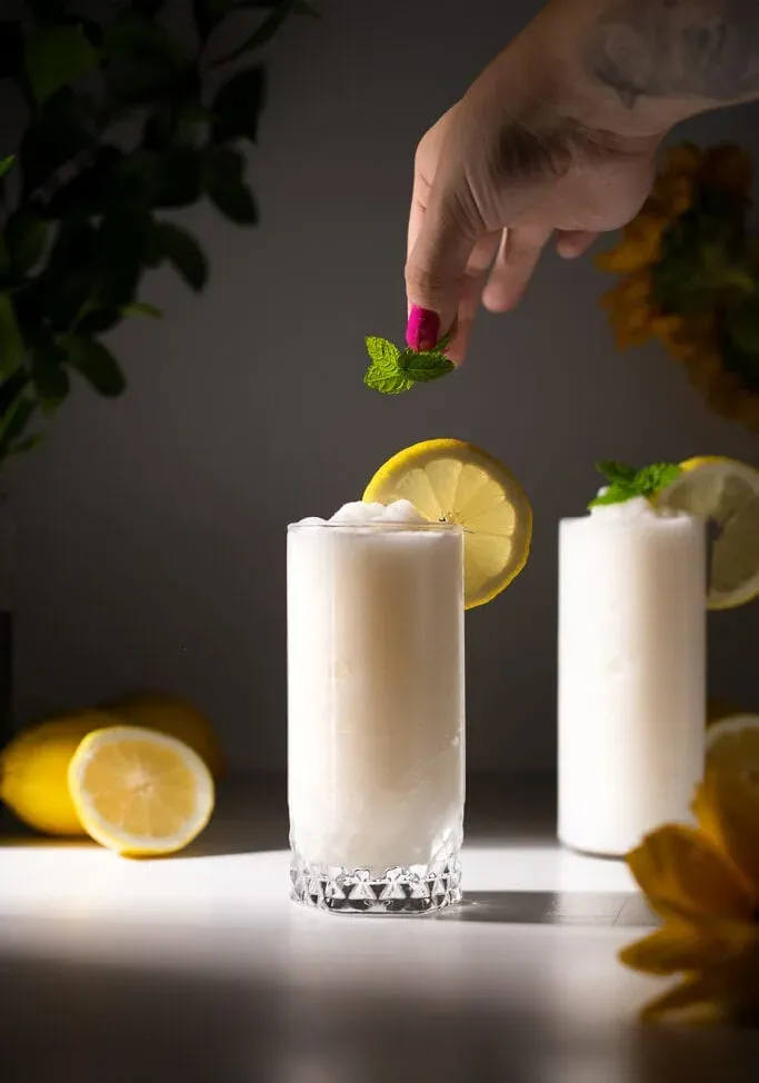 ruka pridávajúca vetvičku mäty do mrazeného nápoja.' loading='lazy' title=