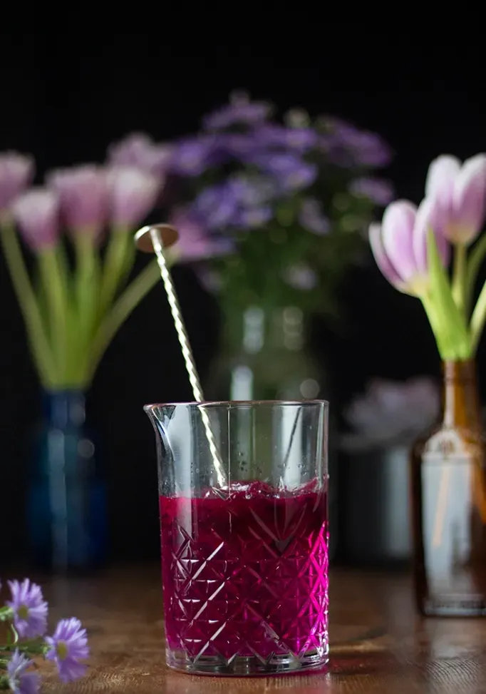 mieszając szklankę wypełnioną ciemnoróżowym płynem i łyżką barową.' loading='lazy' title=