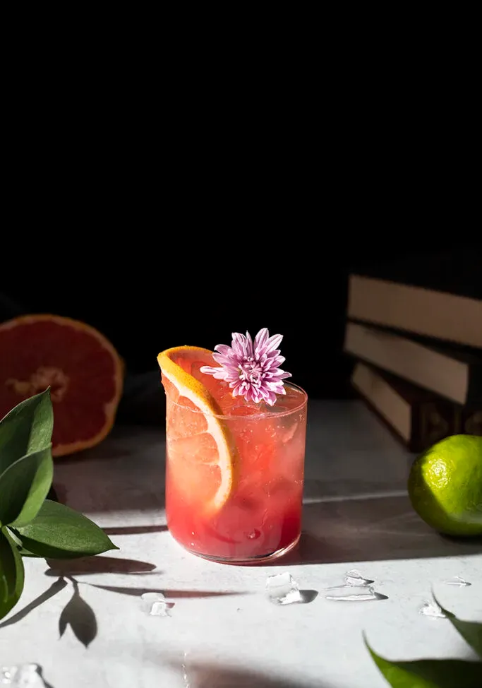 bebida rojiza con una rodaja de pomelo junto a medio pomelo y una lima.' title=