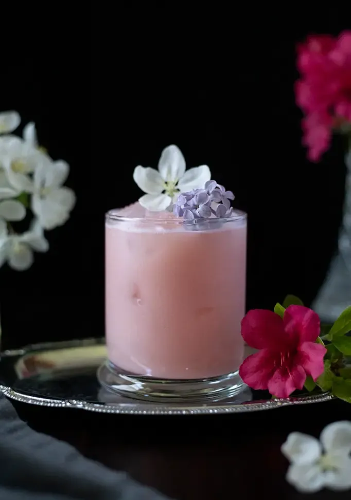 jasnoróżowy napój na srebrnej tacy, z naciskiem na dekorację z fioletowych kwiatów bzu' loading='lazy' title=