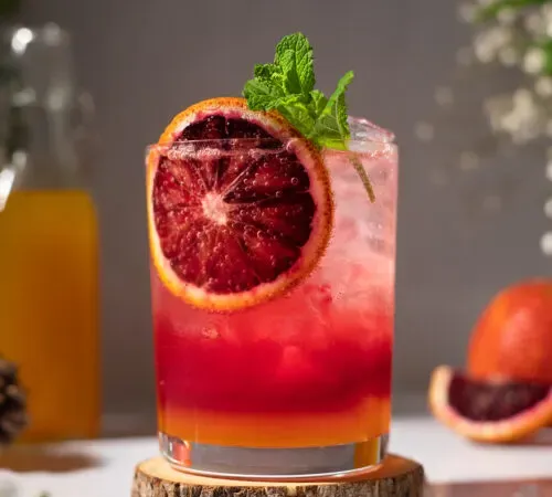 una bebida roja con una rueda de naranja sanguina sobre una montaña rusa de madera.' title=