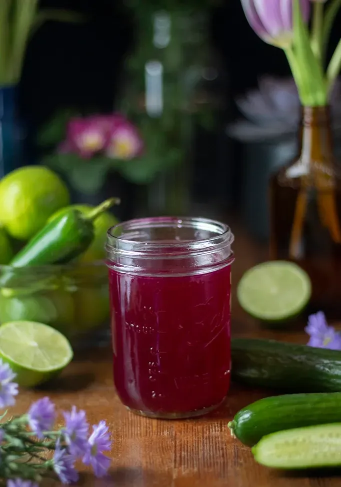 Einmachglas voller rosa Sirup neben Gurken und Limetten.' title=