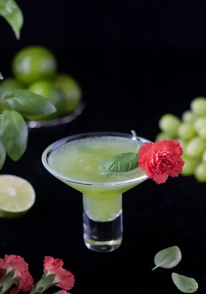 Grüner Martini mit Basilikumblatt und rosa Blumengarnitur.' loading='lazy' title=