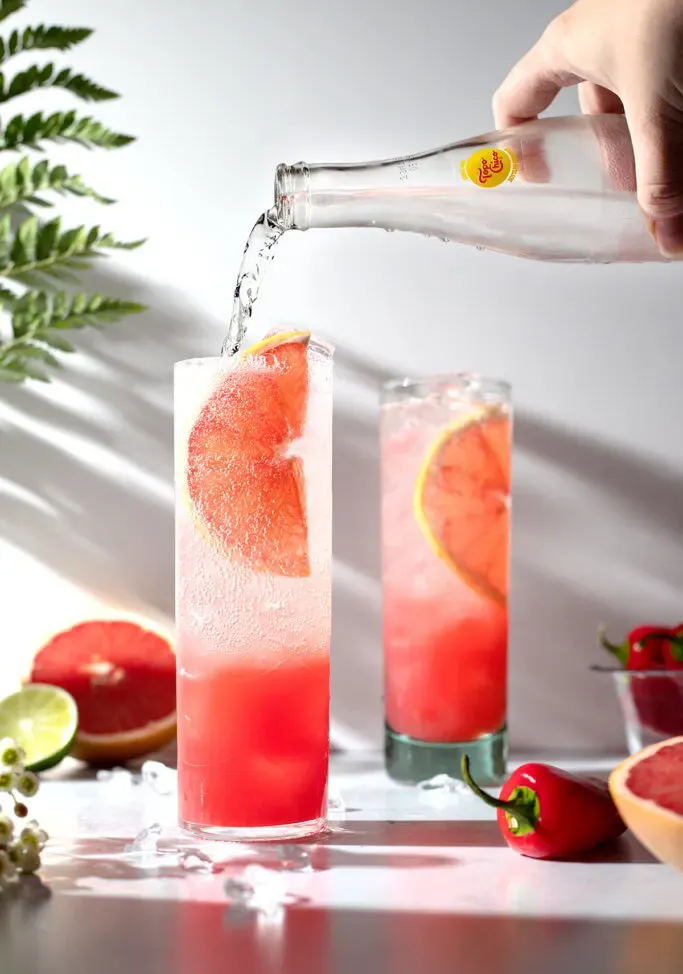 vertiendo agua con gas en bebidas rosadas en vasos altos.' loading='lazy' title=