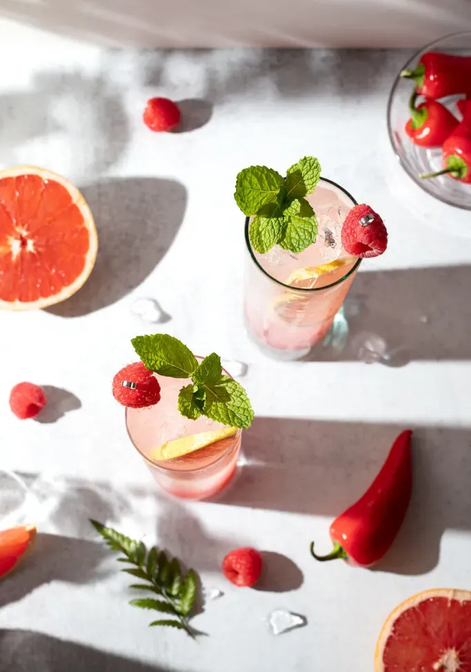 vista aérea de bebidas burbujeantes rosadas adornadas con frambuesas y menta.' title=