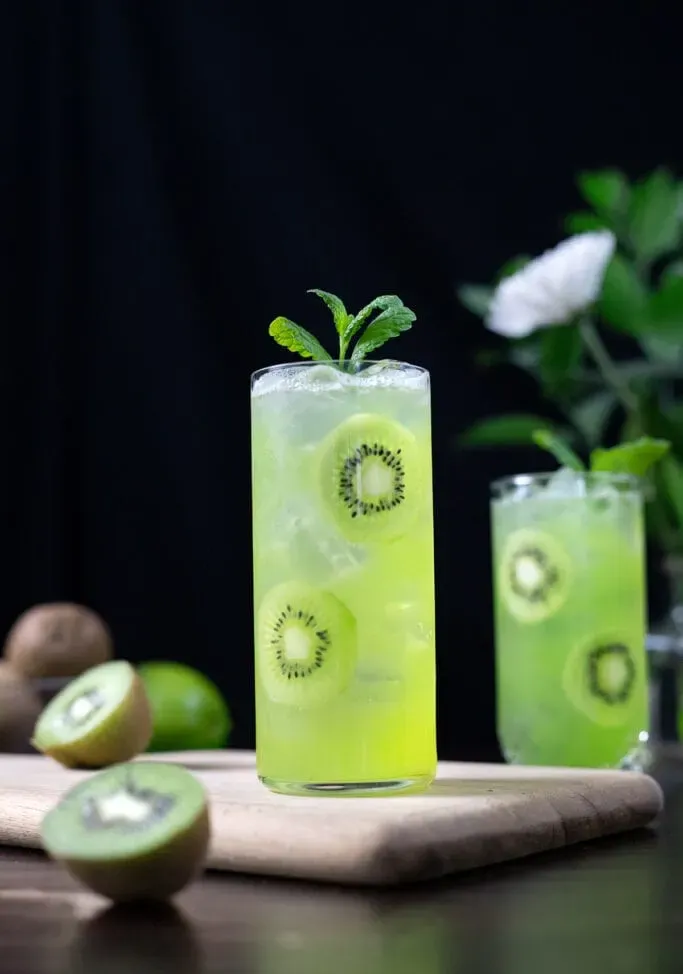 copo alto cheio de líquido verde e fatias de kiwi.' title=