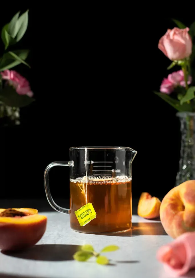 tasse à mesurer en verre remplie de thé vert à côté des pêches.' title=