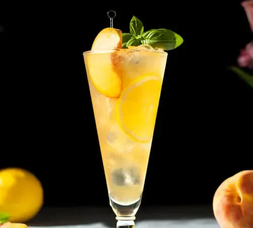 grand verre rempli de limonade au thé vert pêche et d'une tranche de pêche.' title=