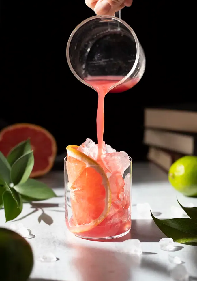 vertiendo jugos rosados ​​en un vaso bajo lleno de hielo.' loading='lazy' title=