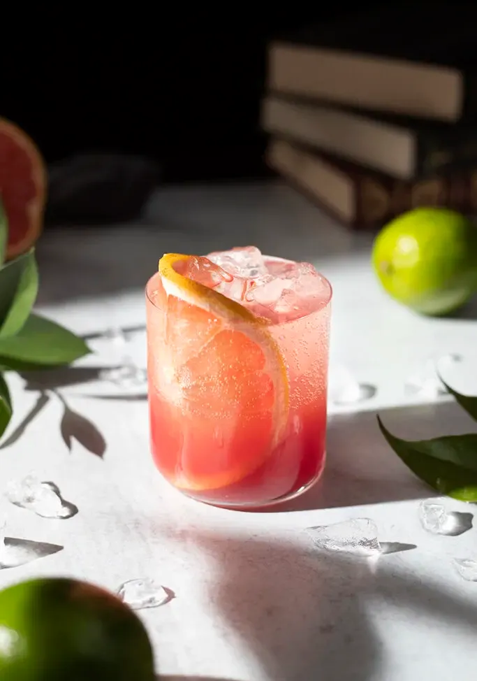 un vaso bajo lleno de una bebida rosa burbujeante y una rodaja de pomelo.' loading='lazy' title=